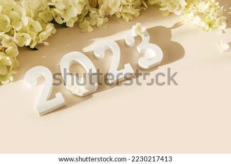 White wooden number 2023 on pastel beige background with flowers. Top view, flat lay. Happy New Year 2023.