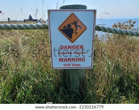A sign in English and French warning of the danger ahead as there is a large cliff.