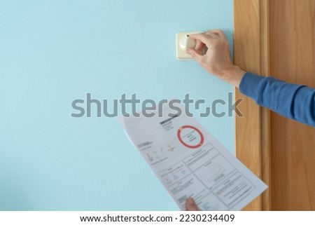 Man with energy bill in hand modifying the temperature on the heating thermostat. Energy crisis concept. Inflation for families. Royalty-Free Stock Photo #2230234409