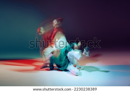 Portrait of young man and woman dancing hip-hop isolated over dark blue background in neon with mixed lights. Concept of movement, youth culture, active lifestyle, action, street dance, ad