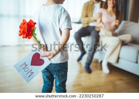 Cute little boy son congratulating his mom happy woman with Mothers day, giving her handmade greeting postcard with red heart at home. Family holidays concept.