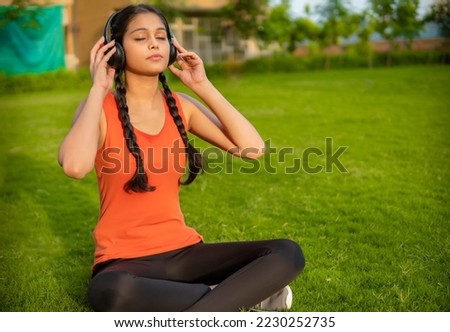 Outdoor image of Asian, an Indian young woman listening music with headphones while doing meditation in outdoor at the park. 