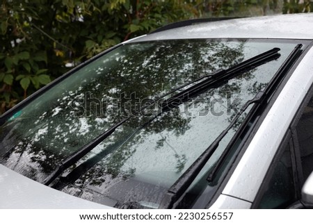 Wipers cleaning raindrops from car windshield outdoors