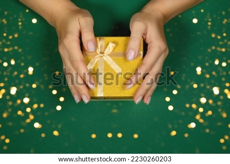 Female hands are holding a gift box with a golden bow on a green background. Flat style.