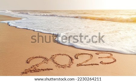 The year 2023- handwriting on sand beach, Happy New Year coming concept. White waves are lapping toward the shore. Royalty-Free Stock Photo #2230264211