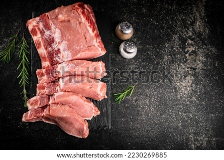 Pieces of raw pork on a stone board with rosemary and spices. On a black background. High quality photo