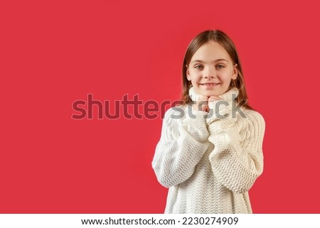 Portrait of a happy pretty girl in a white sweater on a red background, close-up portrait isolated. The girl smiles. Empty space for inscriptions, text or congratulations.