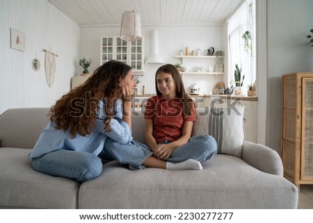 Teenage daughter sharing secrets with young loving supportive mother, parent mom talking chatting with adolescent girl while sitting together on sofa at home. Healthy parent-teen relationships Royalty-Free Stock Photo #2230277277