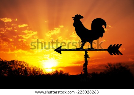 Rooster weather vane against sunrise with bright colors in clouds, concept for early morning wake up Royalty-Free Stock Photo #223028263