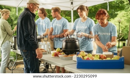 Team of Young Volunteers Helping in a Local Community Food Bank, Handing Out Free Food to Low-Income People in a Park on a Sunny Day. Charity Workers Work in Humanitarian Aid Donation Center. Royalty-Free Stock Photo #2230295099