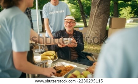 Happy Middle Aged Man with Disabilities Using Wheelchair Receiving a Charity Meal from a Humanitarian Aid Food Bank. Volunteers Helping People in Need in Local Community. Royalty-Free Stock Photo #2230295115