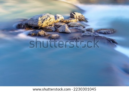 Pile of rock, in the middle of a mountain river, with turquoise waters. Long exposure photo.
Before sunset, in the southern French Alps.