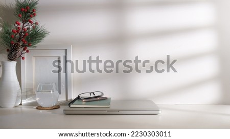 Bright modern workplace with picture frame, laptop, books and glass of water on white table.