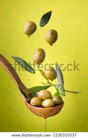 ladle with olives and oil on a green background. Olives, extra virgin olive oil and olive leaves float in the air Royalty-Free Stock Photo #2230310337