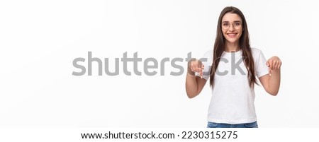 Click here. Portrait of brunette gorgeous young woman in glasses, pointing fingers down to show advertisement, smiling pleased, suggest visit link, recommend download or subscribe, white background. Royalty-Free Stock Photo #2230315275