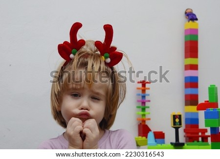 Sweet boy 4 years old with long hair grimaces. The child plays with the designer. Waiting for Christmas gifts. A boy dressed reindeer. Dear friend of Santa Claus. Isolate on white 