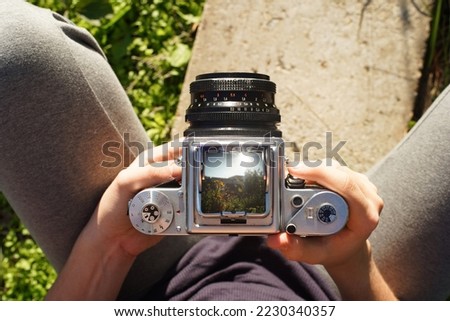  A photographer holding a vintage analog photo CAMERA focusing ajusting taking pictures outside looking through a large square format viewfinder mechanical settings solid metal cogs garden background