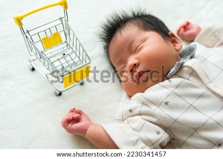 A photograph of a sleeping one-month-old 0-year-old newborn, a shopping cart, and a white background taken obliquely from above