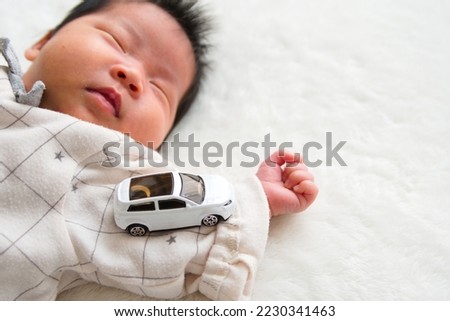 A picture of a 1 month old 0 year old newborn sleeping and a car on his arm and a white background