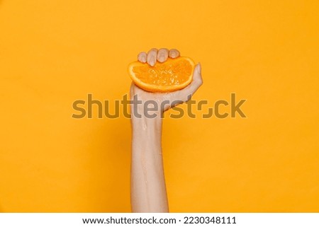 Female hand squeezing half of orange isolated over yellow studio background indoors Royalty-Free Stock Photo #2230348111