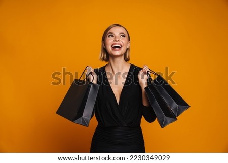 Portrait of young excited woman holding shopping bags and looking up standing isolated over orange background Royalty-Free Stock Photo #2230349029