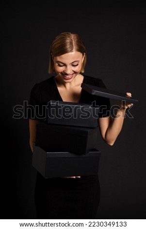 Beautiful woman smiling while opening black gift boxes isolated over black studio background