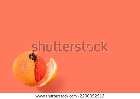 Christmas miracle concept, christmas red ball inside grapefruit hanging over orange background, concept of new year miracle and decorations, unusual holiday decoration for christmas, picture postcard