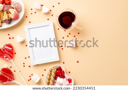 Valentine's Day concept. Top view photo of white photo frame saucers with confectionery cookies candies lollipops and heart shaped glass of beverage on isolated beige background with empty space