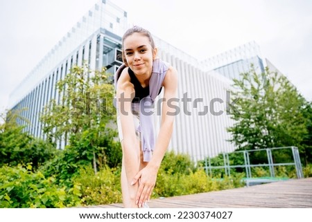 Young woman in sportswear workout, warming up, stretching on modern urban rooftop with green plants outdoor at summer.
