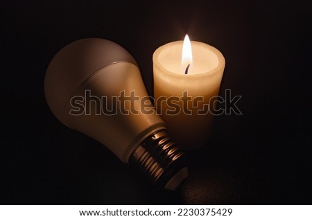 Switched off light or not glowing energy saving LED bulb liying near a burning candle in darkness. Blackout city, electricity off, load shedding, energy crisis or power outage, symbolic image. Royalty-Free Stock Photo #2230375429