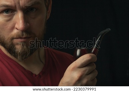 Lumberjack brutal beard muscled man in red shirt with smoking tube pipe standing on dark background