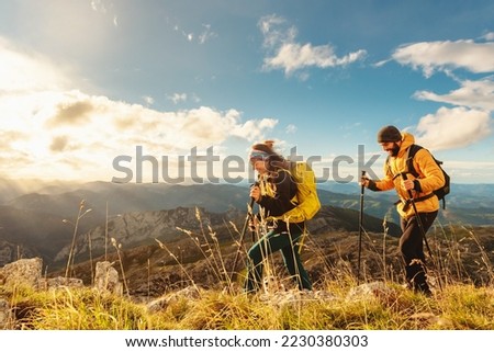 two mountaineers, male and female, trekking up a mountain at sunset. hikers equipped with backpacks, trekking poles and warm clothing walking up the mountain. Royalty-Free Stock Photo #2230380303