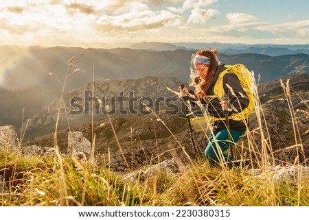 caucasian woman equipped with backpack, warm clothes and trekking poles hiking alone on a mountain. sports and outdoor adventures.