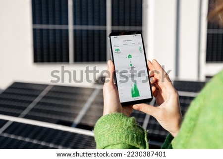Woman monitors energy production from the solar power plant with mobile phone. Close-up view on phone screen with running program. Concept of remote control of solar energy production Royalty-Free Stock Photo #2230387401