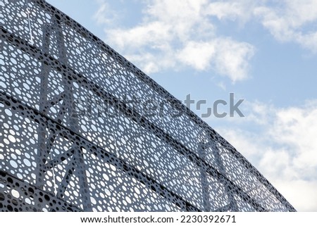 Decorative metal wall with round holes pattern under cloudy blue sky, abstract industrial background photo Royalty-Free Stock Photo #2230392671