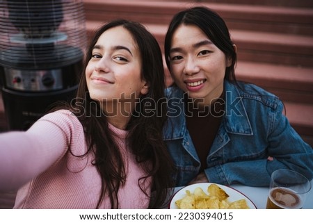 Shot of two happy girls taking a selfie while they are a beer and a snack