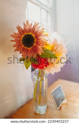 Flowers in a vase on a wooden table with a reserved sign. The walls and window have a rustic vintage feel. There is soft window light.