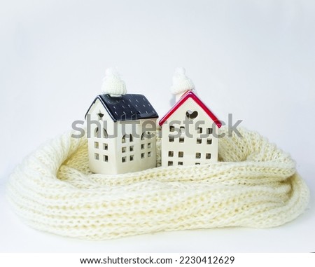 Photo on a white background two houses in a white knitted scarf and a warm cap.  The concept of warmth in the house is a cozy atmosphere.  Winter mood Christmas and New Year.  Space for copy text.
