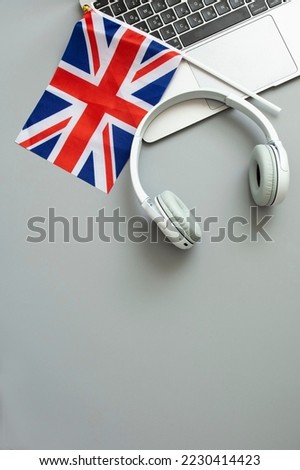 The concept of online learning English, foreign languages, distance education, knowledge, modern technologies for study. Laptop, English flag, headphones. Grey background. Vertical. Nobody. Royalty-Free Stock Photo #2230414423