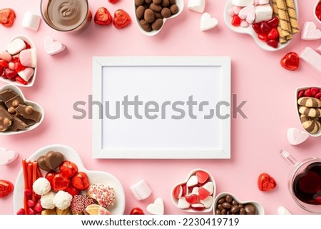 Valentine's Day concept. Top view photo of white photo frame heart shaped plates with sweets candies and glasses with drinking on isolated light pink background with empty space