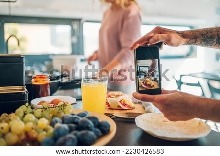Close shot of a man hands holding a smartphone while photographing breakfast in the kitchen. Husband and wife at home on a weekend preparing food and enjoying.