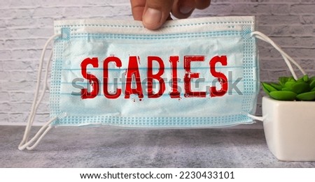 The words Scabies is written on white paper on a grey background near a stethoscope. Medical concept