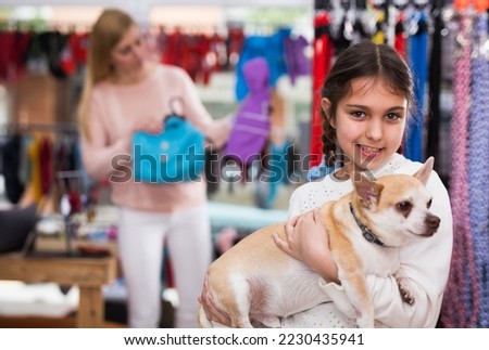 Positive european girl child with her dog in pet store during shopping with her mother
