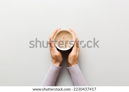 Minimalistic style woman hand holding a cup of coffee on Colored background. Flat lay, top view cappuccino cup. Empty place for text, copy space. Coffee addiction. Top view, flat lay.