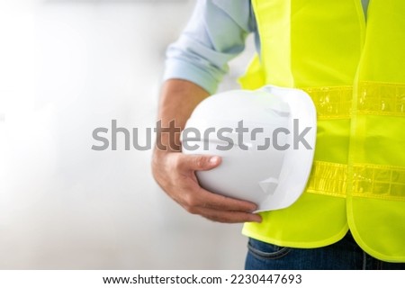 The engineer is holding a hard hat wearing a yellow vest and standing ready for work safety on site. Royalty-Free Stock Photo #2230447693