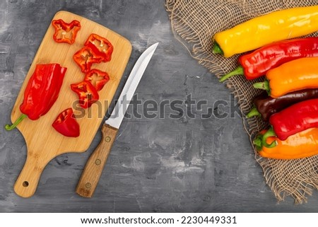 Fresh sweet pepper (bell pepper) on a cutting board with a knife. Chopped pepper pieces are ready to cook. On a gray background, top view.