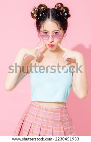 Portrait of beautiful young Asian happy woman in blue cute fashion dress wear sunglass smiling and posing on isolated pastel pink color background empty space.