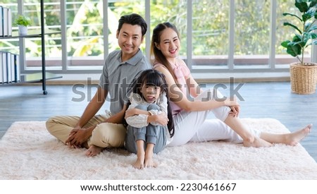Millennial Asian happy family father mother and little girl daughter in casual outfit sitting laying lying down on fluffy carpet floor smiling posing together taking photograph in living room at home.