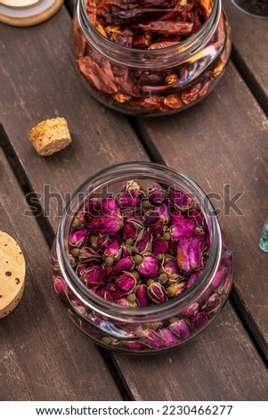 Glass jar with cork lids filled with dried tea roses on unvarnished dark wood planks