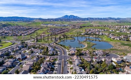 Aerial photography over a suburb in Brentwood, California with homes, lake and green hills in the foreground and a mountain in the background